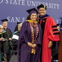 A woman and man in Commencement regalia smile at the camera